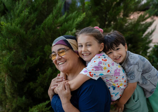 retrato de lindos hermanos jugando con su abuela frente a un pino en el patio trasero - grandmother generation gap senior adult granddaughter fotografías e imágenes de stock