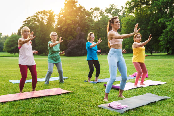 seniorinnen trainieren mit fitnesstrainer im park - yoga exercising outdoors group of people stock-fotos und bilder