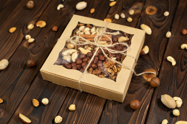 istock Nuts of different varieties in a box on a structural wooden background top view. Assorted nuts in a paper box. 1357132899