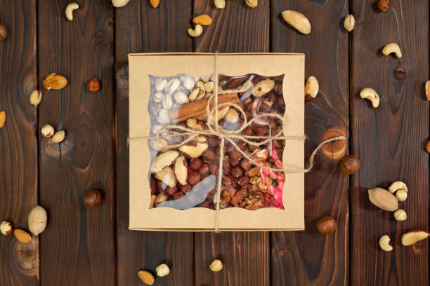 istock Nuts of different varieties in a box on a structural wooden background top view. Assorted nuts in a paper box. 1357132991
