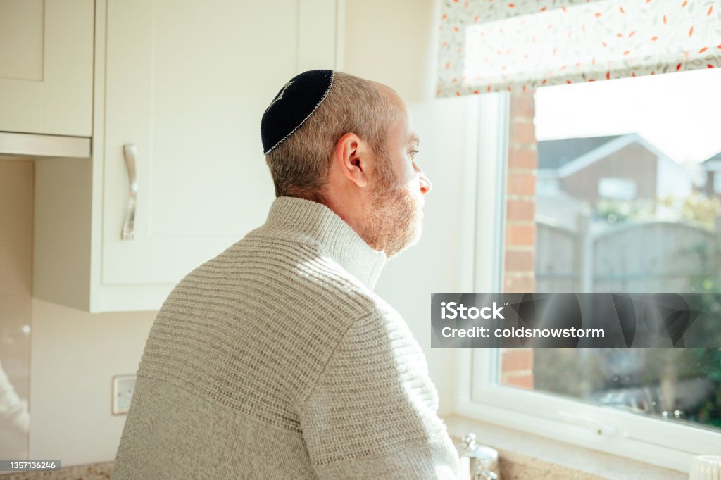 Jewish man wearing skull cap at home Color image depicting a mid adult Jewish man in his 30s wearing a traditional Jewish skull cap (with star of David design). The man has a beard and is relaxing at home. Room for copy space. 30-39 Years Stock Photo