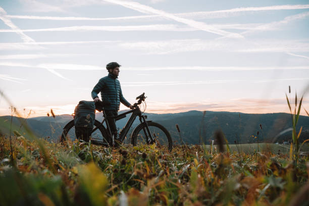E-mountain biker relaxes in meadow, at sunrise