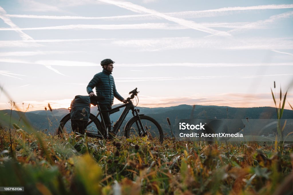 E-mountain biker relaxes in meadow, at sunrise He looks off to distant scene Germany Stock Photo