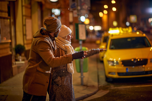 Smiling Man and woman in night  street calling taxi.