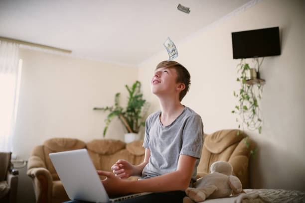 freelance teenager recounts money earned online on laptop and happy with earnings. boy studies online and earns money from comfort of home. child counting money showing it friends on conference call adolescente independiente relata el dinero ganado en línea en una computadora portátil y feliz con las ganancias. el niño estudia en línea y gana dinero desde la comodidad de su hogar. niño contando dinero mostrándolo a sus amigos en una conferencia