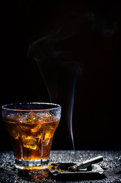 Glass of cold alcohol drink and cigarette Glass of cold alcohol drink and cigarette over black background glass of bourbon stock pictures, royalty-free photos & images