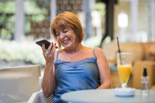 mujer sosteniendo un teléfono inteligente y sonriendo - cafe table outdoors speaker fotografías e imágenes de stock