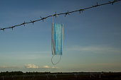 Concept image of a protective surgical mask on barbed wire against a landscape background.