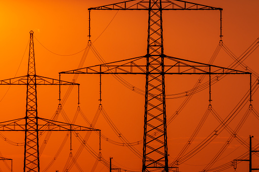 Electricity pylons and wires against an orange sunset.