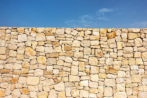 Old beige brown masonry wall of stones and blue sky background. Low angle view.