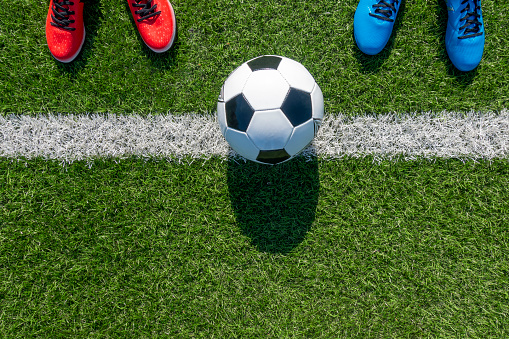 Soccer football background. Soccer ball and two pair of football sports shoes on artificial turf soccer field.