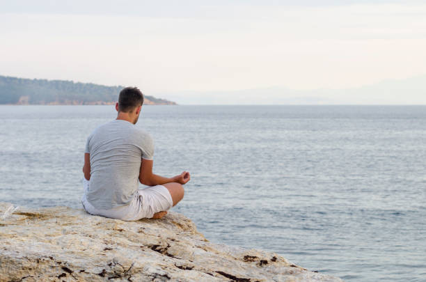 istock Young man sitting on the coast and meditating 1357169469