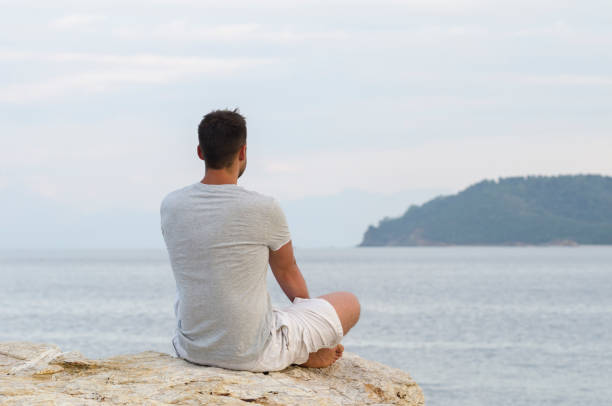 istock Young man sitting on the coast and meditating 1357169608