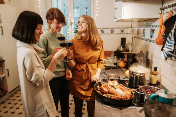 three women drinking wine while preparing christmas dinner at home - wine dinner party drinking toast imagens e fotografias de stock