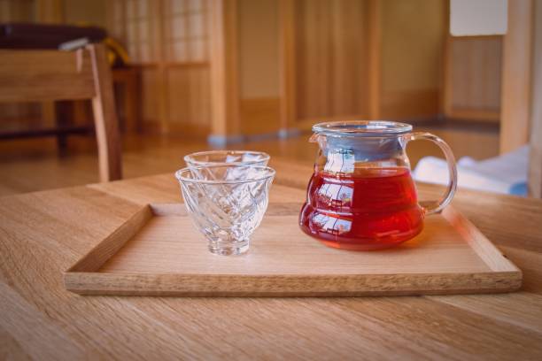 tasses à thé en verre élégantes et douces et théière avec tisane rooibos sur table kotatsu en bois japonais traditionnelle sur fond minimaliste flou dans le club de santé spa hot springs. loisirs de bien-être - green tea tea zen like japan photos et images de collection