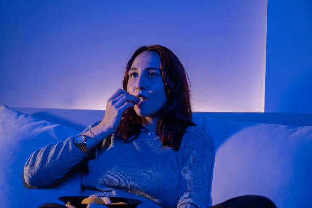 istock redhead young woman eating fruit while watching tv 1357173087