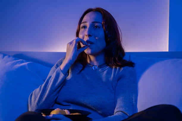 istock redhead young woman eating fruit while watching tv 1357173175