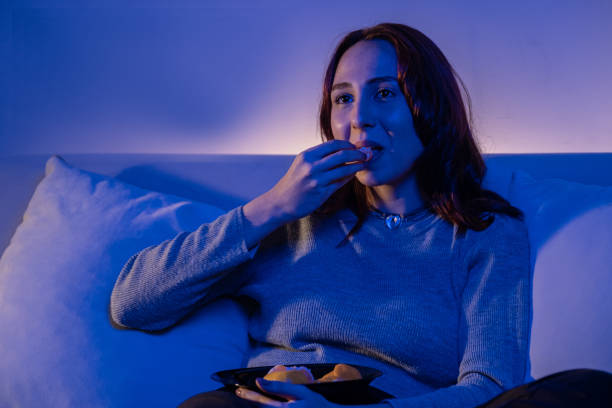 istock redhead young woman eating fruit while watching tv 1357173176