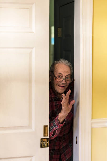 istock Grandpa Peeking and Waving Hand Through Doorway 1357181728