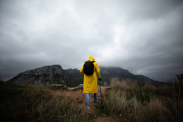 istock Hiker in a yellow raincoat climbing a mountain 1357182726