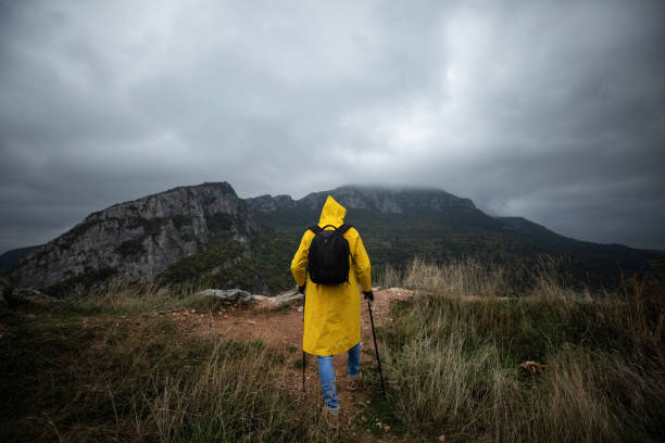 istock Hiker in a yellow raincoat climbing a mountain 1357184268