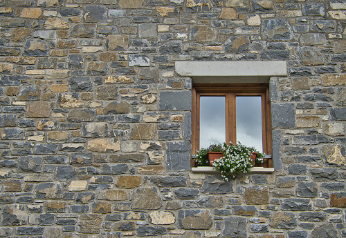 Stone facade with window detail decorated with white flowers. Rural house in the Pyrenees.