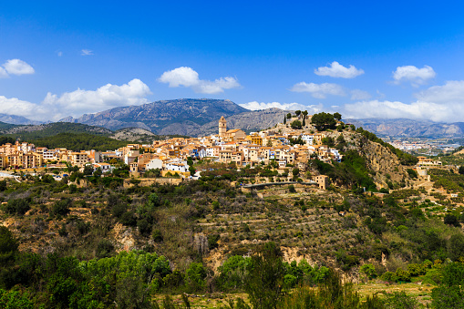 Beautiful mountain village of Polop de la Marina, houses with tiled roofs, church tower against the backdrop of beautiful nature, mountains and sky, Spain