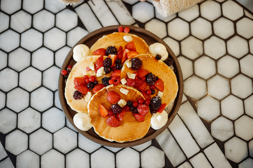 The appearance of tiny pancakes with honey, raspberries and blackberries on a white plate