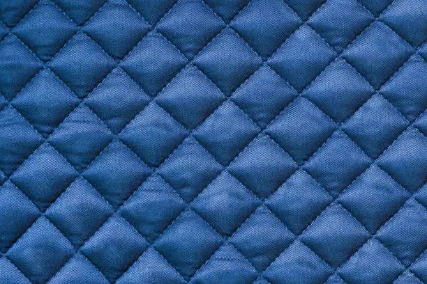 Quilted fabric. Background blue cloth sewn into the cell, stitching. Texture of the blanket, blue textile. Double faced pre quilted cotton fabric diamond solids
