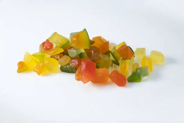 Photo of Portion of candied fruit or fruit comfit in small cubes and multicolored, stacked on a white background