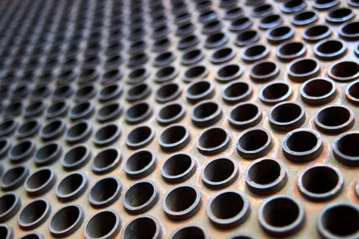 Tube sheet or plate of heat exchanger or boiler selective focus shot at an angle closeup texture industrial background, with insoluble hard mineral deposits salts scale and corrosion, with copyspace.