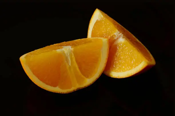 Isolated ripe orange fruit slices in macro view with texture. Black background. white and yellow orange peel. vitamin and healthy eating concept. vegetarian lifestyle. still life image
