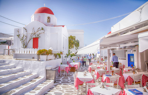 Tables in a tavern in front of typical red top church in Mykonos town, Cyclades, Greece