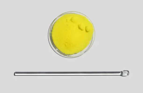 Photo of Potassium Chromate Powder in Chemical Watch Glass place next to stirring rod. Closeup chemical ingredient on white laboratory table. Top View