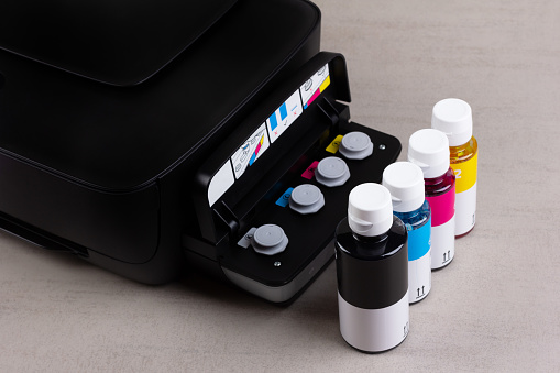 inkjet four-color printer with continuous ink supply and ink bottles for refilling on grey background close-up