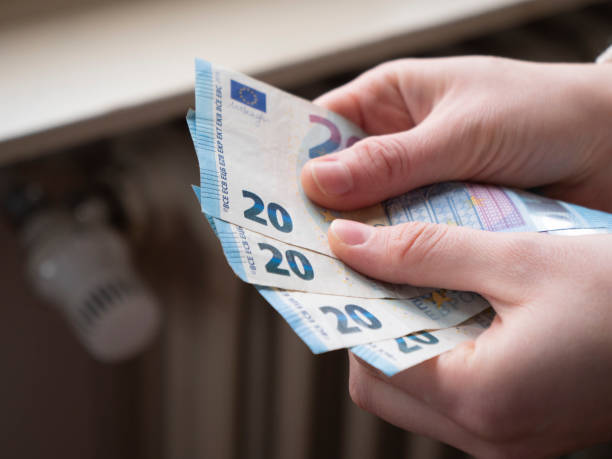 gas price increases, hands hold euro banknotes next to the radiator, house heating rising price concept, increased gas value stock photo