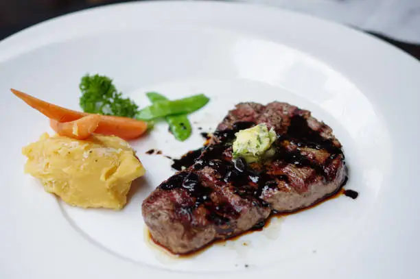 Grilled steak with mashed potatoes and black pepper sauce with white round plate