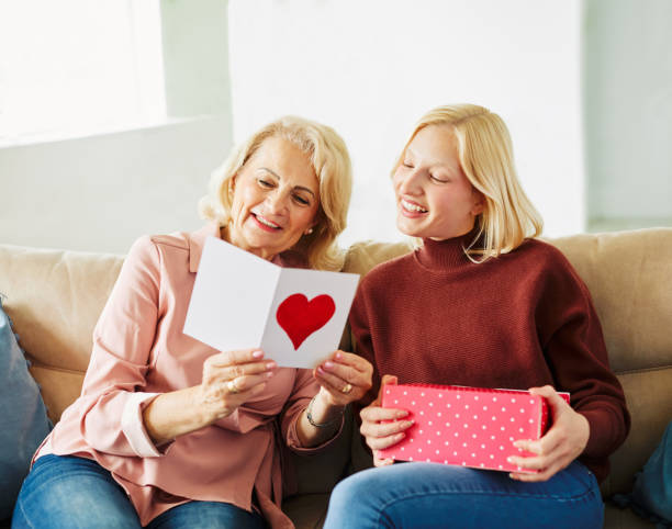 mother daughter grandmother granddaughter gift present greeting card birthday mother day family greeting card box love celebration holiday Daughter or granddaughter surprises her mother or grandmother with present on mother's day or birthday at home senior birthday card stock pictures, royalty-free photos & images