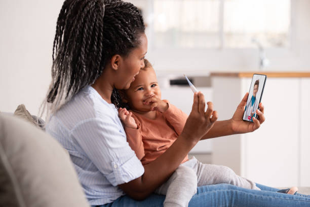 Online consultation with doctor. Woman and baby daughter using a smartphone to communicate with the doctor, showing thermometer display to her. telemedicine stock pictures, royalty-free photos & images