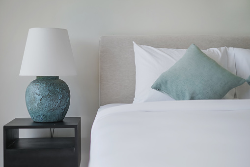 Shot of clean minimalist bedroom design. There's a turquoise loose pillows and a nice ceramic vase side lamp.
