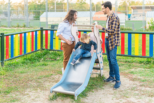 Full length view of a gay male couple playing with their children on the slider of a playground