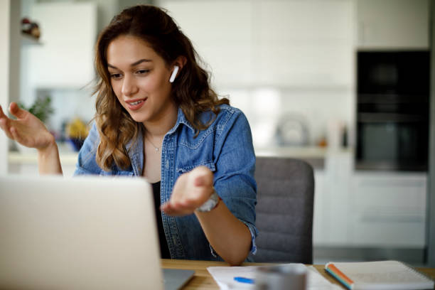 Smiling young woman with headphones having video call on laptop computer at home stock photo
