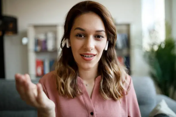 Photo of Young smiling woman with bluetooth headphones having video call at home