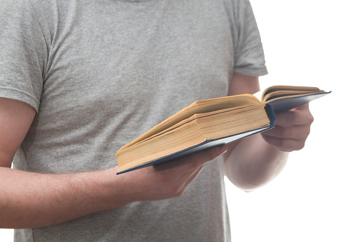 A man holding open and reading an old blue book on a white background.