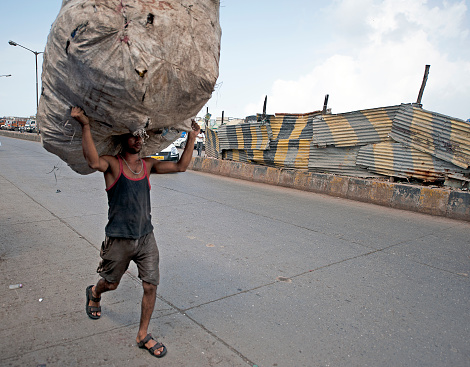 Plastic recycling worker carries headload of bottles, Dharavi slums, Mumbai, India, India, land of contrasts, colours and sounds from its religious devotions, colourful costumes and dress, picturesque and multicolored landscapes to its multicultural population that clamours in its towns and cities