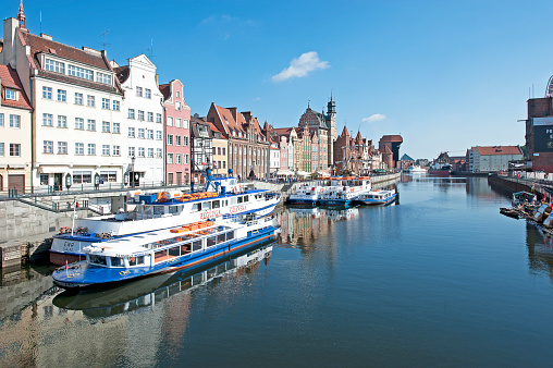 Embankment of the Motlawa River in Gdansk. Old brick houses and crane. Tourist ship in the foreground