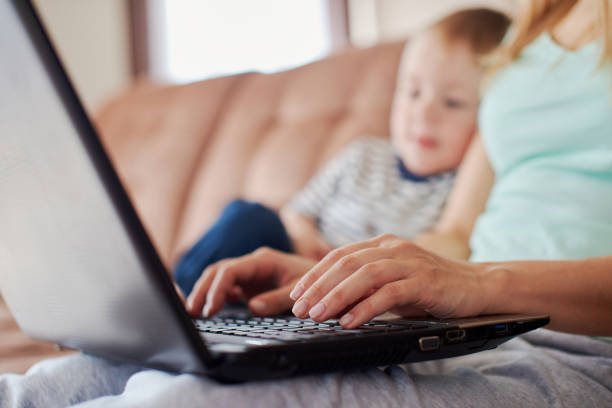 Close up of mother's hand typing on keyboard while baby is leaning on her stock photo