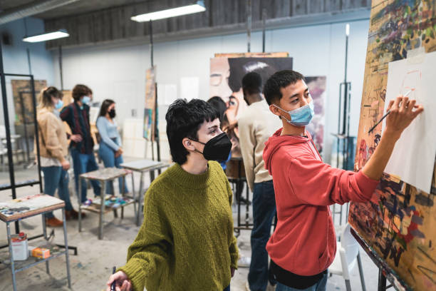 des élèves multiraciaux peignent à l’intérieur de la salle d’art en portant des masques de sécurité - focus sur le dos du garçon - artist child artists canvas indoors photos et images de collection