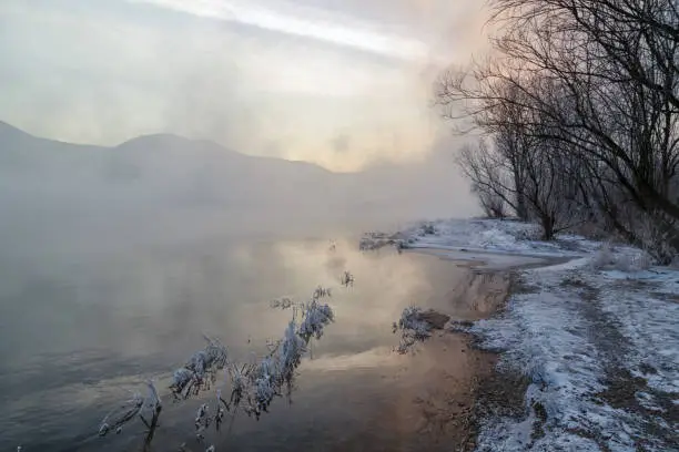 Photo of Winter landscape, river with icy banks, mountains in the fog.