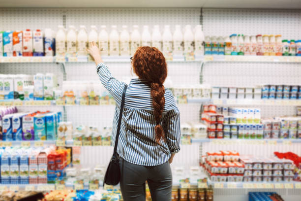 現代のスーパーマーケットで乳製品を選ぶ背中からストライプのシャツを着た若い女性 - department store ストックフォトと画像
